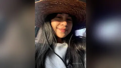 Smiling woman in a white top and wide-brimmed straw hat enjoying a sunny outdoor moment.