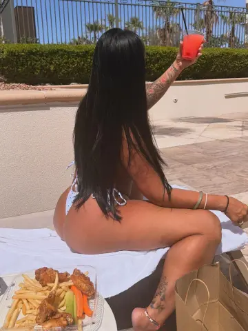 Woman in white bikini relaxing on a sunlit patio with a refreshing red drink and snacks.