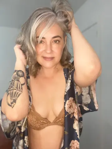 Woman with grey hair in a floral kimono and lace bra posing in a bright indoor setting.