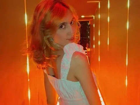 Young woman in a white sleeveless dress posing in a warm, glowing hallway with vertical fairy lights.