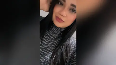 NiaCorelli poses with her hand behind her head, wearing a black and white patterned turtleneck and showing her long dark hair.