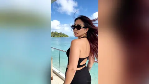 Stylish woman in black swimwear and sunglasses enjoying a sunny tropical beach vacation by turquoise ocean waters.