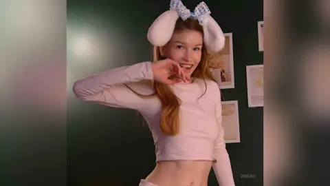 Smiling young woman in a white long-sleeve crop top and bunny ears posing in a cozy room.