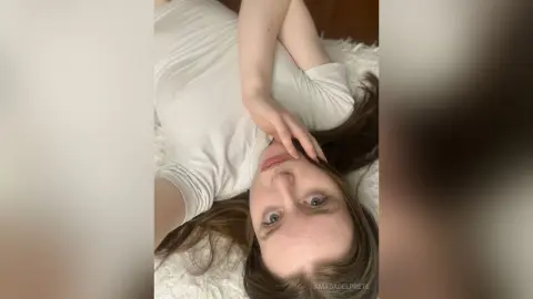 Young woman in a white tank top relaxing on a cozy white rug in a bright, peaceful indoor setting.