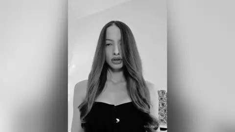 Young woman with long hair wearing a black strapless top in a moody black and white portrait.