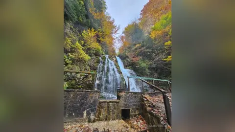 Serene autumn waterfall cascading through a lush forest with colorful fall foliage in a peaceful mountain setting.