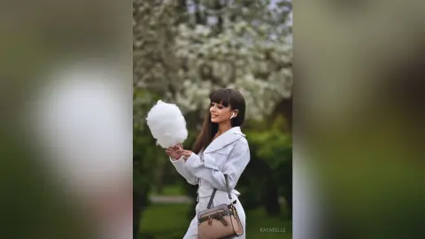 Young woman in a white blazer holding cotton candy in a blooming spring garden.