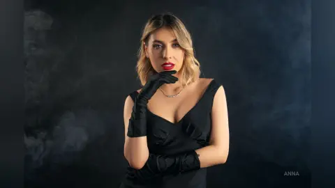 Elegant woman in a black evening dress and long gloves posing against a moody dark background.