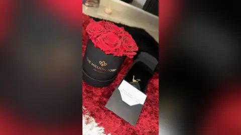 Elegant red rose bouquet in a black luxury gift box on a soft red textured surface.