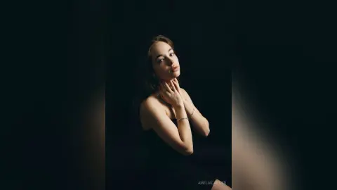 Elegant woman in a black dress posing against a dark background with moody, cinematic lighting.