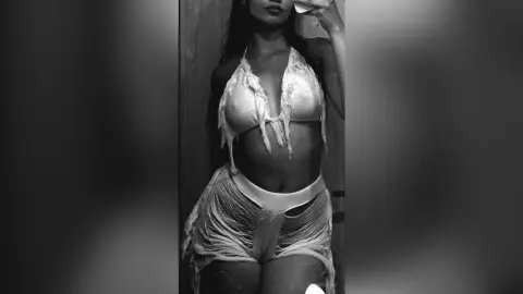 Young woman in a white fringed crochet bikini set posing for a moody black and white mirror selfie.