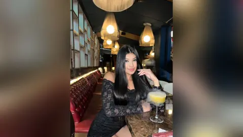 Elegant woman in a black lace dress enjoying a cocktail in a moody, upscale lounge setting.