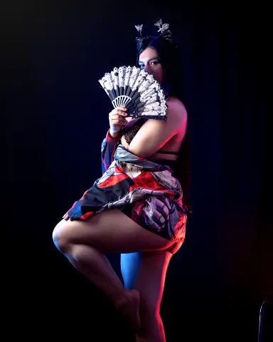 Mysterious woman in a patterned kimono holding a decorative fan against a dark, moody background.