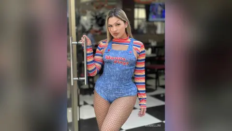 Young woman in a blue graphic bodysuit and fishnet tights posing confidently in a modern indoor setting.