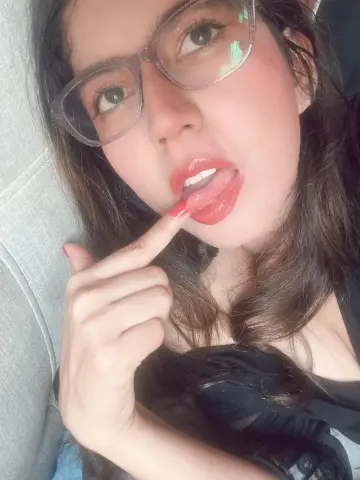 Zharid_Parker wearing glasses and red lipstick, biting her finger while lying on a couch.