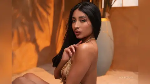 Beautiful woman in gold chain bikini relaxing in warm sunlight against a sandy desert background.