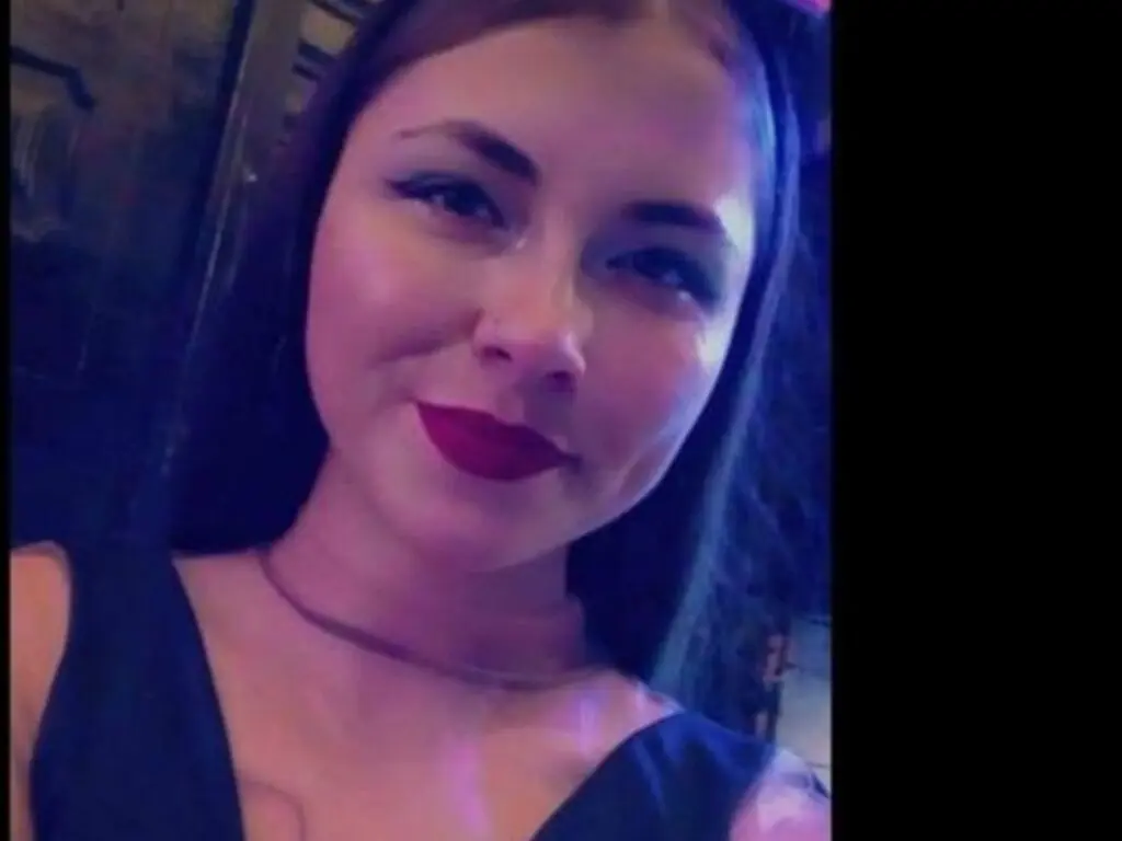 Smiling young woman in a black dress with red lipstick posing in moody blue lighting.