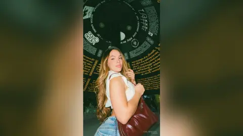 Young woman in a white top and denim jeans posing under a dark graphic ceiling in a moody indoor setting.