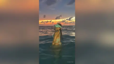 Young woman in a mint green bikini and visor enjoying a serene sunset swim in the ocean.