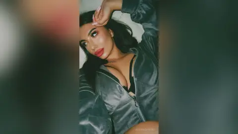 Glamorous woman in a grey velvet zip-up jacket relaxing with a moody, confident expression.