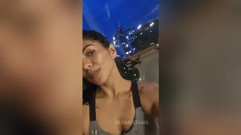 Young woman in grey athletic tank top posing outdoors at night under blue lighting.