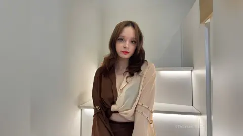 Young woman in a stylish brown and cream blouse sitting on modern white stairs in a bright minimalist room.
