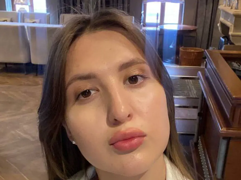 Close-up portrait of a young woman with natural makeup in a bright, modern indoor setting.