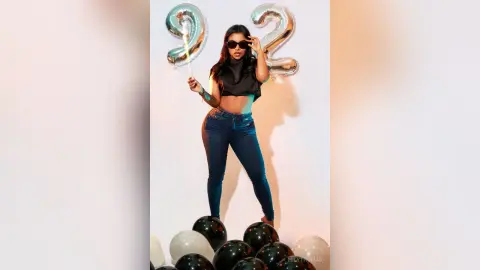 Stylish woman in black crop top and jeans posing with silver number 92 balloons for a birthday celebration.
