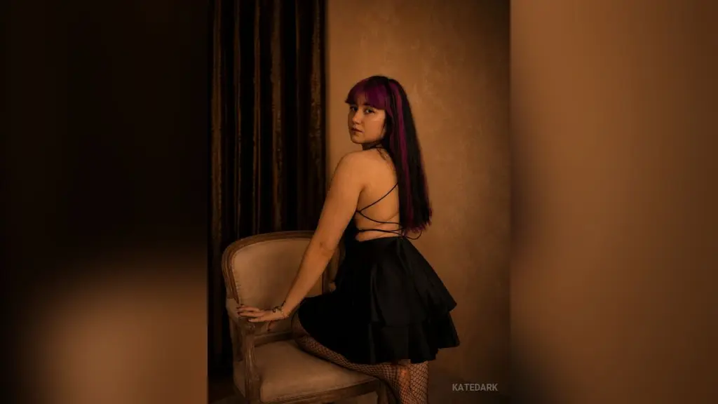 KateDark with purple hair poses in black lace lingerie while looking back over her shoulder.