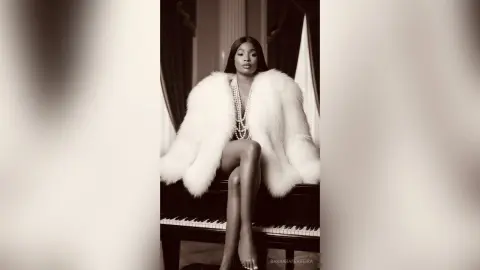 Elegant Black woman in a white faux fur coat and pearl necklace sitting on a piano in a moody black and white setting.