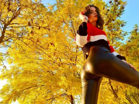 Stylish woman in a red sweater and black leather pants posing under vibrant yellow autumn trees.