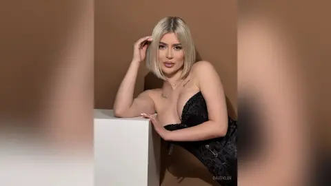 Blonde woman in a black lace corset posing elegantly against a neutral brown background.