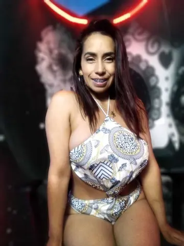 Smiling woman in a white patterned bikini set posing in a dimly lit club setting.