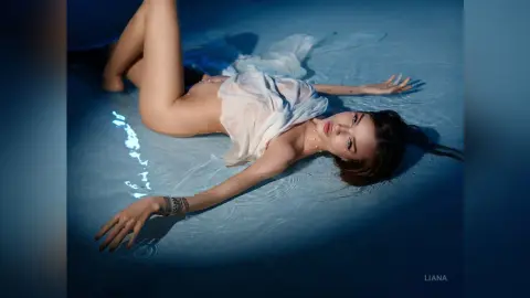 Young woman in a white flowing dress lying in a blue water pool under moody, cinematic lighting.
