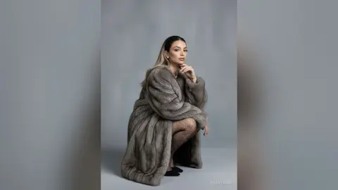 Elegant woman in a luxurious grey faux fur coat posing against a minimalist studio background.