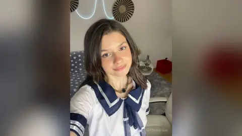 Smiling young woman in a white sailor-style blouse sitting in a cozy, modern living room.