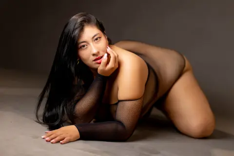 Curvy woman in black sheer lingerie posing gracefully against a dark studio background.