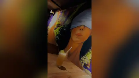 Refreshing iced cocktail on a wooden table in front of a large colorful portrait mural in a moody lounge.