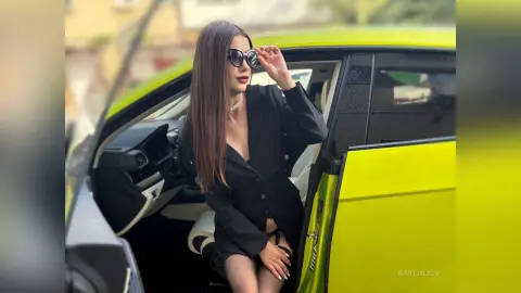 Stylish woman in a black blazer and sunglasses sitting in a bright lime green luxury car.