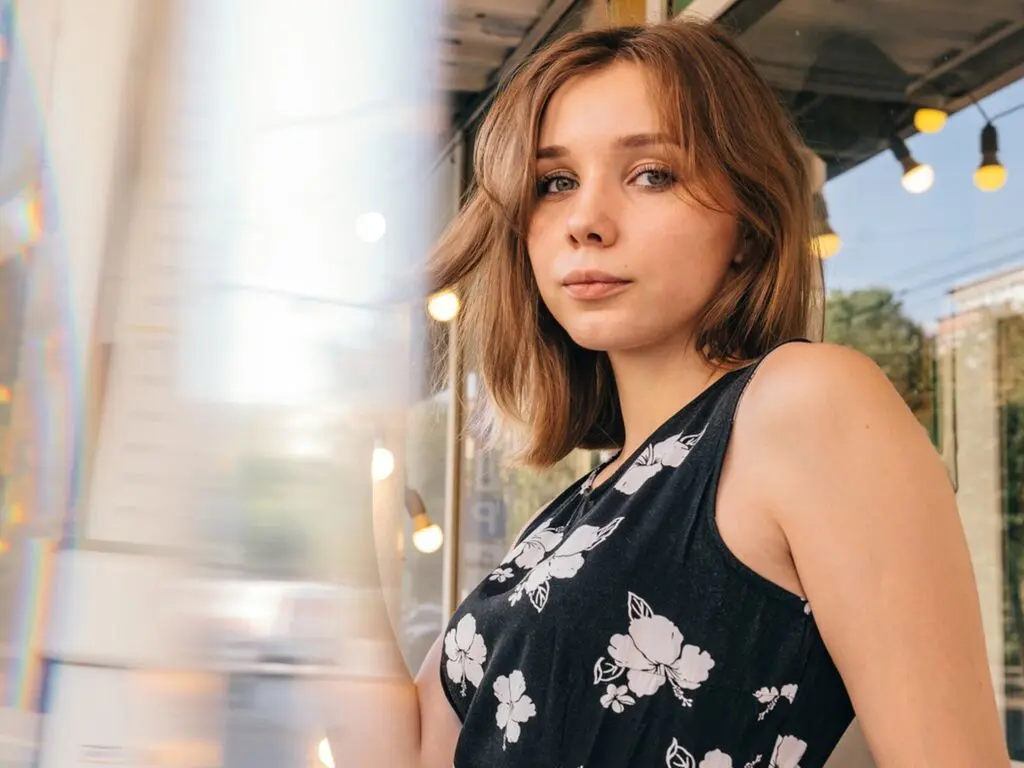 Young woman in a black floral sleeveless top sitting at an outdoor cafe with warm bokeh lighting.