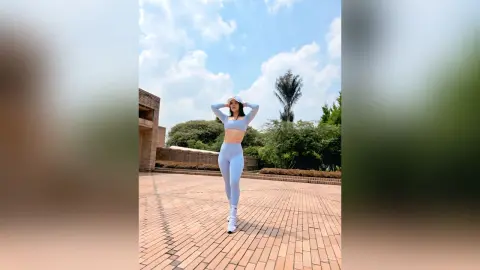 Fit woman in light blue yoga set posing confidently on a sunny brick courtyard under a blue sky.