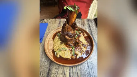Roasted lamb shank served on creamy mashed potatoes with rich gravy in a rustic restaurant setting.
