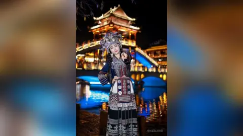 Woman in traditional Chinese Hanfu costume with ornate silver headpiece posing at a night festival by a glowing lake.