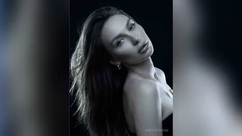 Moody black and white portrait of a brunette woman with long hair in a dramatic studio setting.