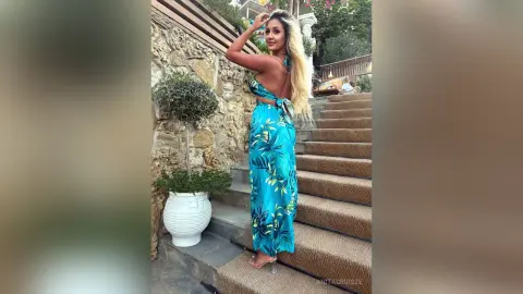 Anita stands on outdoor stone stairs wearing a blue tropical print sundress with a low back and thin straps.
