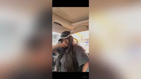 KeianHoz wears a black cap and a dark grey t-shirt while sitting in a car.