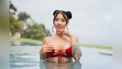 Smiling woman in a red bikini relaxing in a luxury outdoor swimming pool on a bright sunny day.