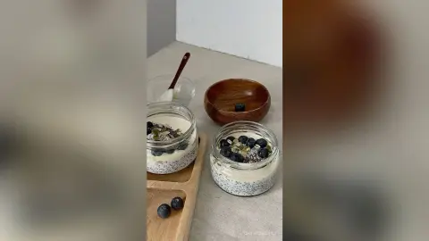 ChristineDavis prepares a healthy breakfast or snack consisting of chia seed pudding topped with blueberries and seeds in glass jars.