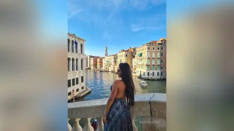 Woman in a patterned sundress overlooking the Venice canal with historic buildings under a blue sky.