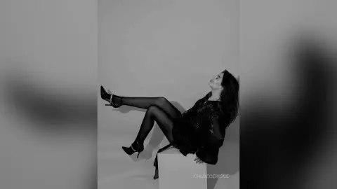Elegant woman in a black dress and heels posing gracefully in a minimalist studio setting.